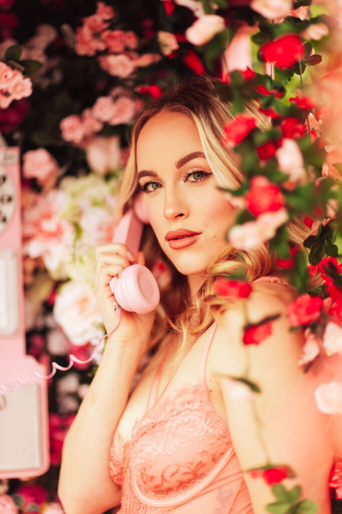 "Romantic boudoir photo in a pink London telephone booth filled with blooming flowers."
"Couple embraces in an intimate moment surrounded by pink-painted telephone booth and floral decorations."
"Soft and passionate boudoir setting with a pink London phone booth and a sea of flowers."