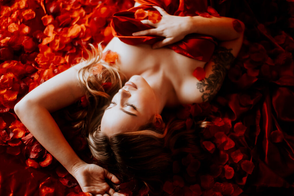 "Luxurious boudoir setting on a red silk bed covered in thousands of red rose petals."
"Sensual moment captured on a velvety red silk bed adorned with a cascade of red rose petals."
"Elegant and romantic boudoir scene featuring a bed covered in red silk and a blanket of rose petals."