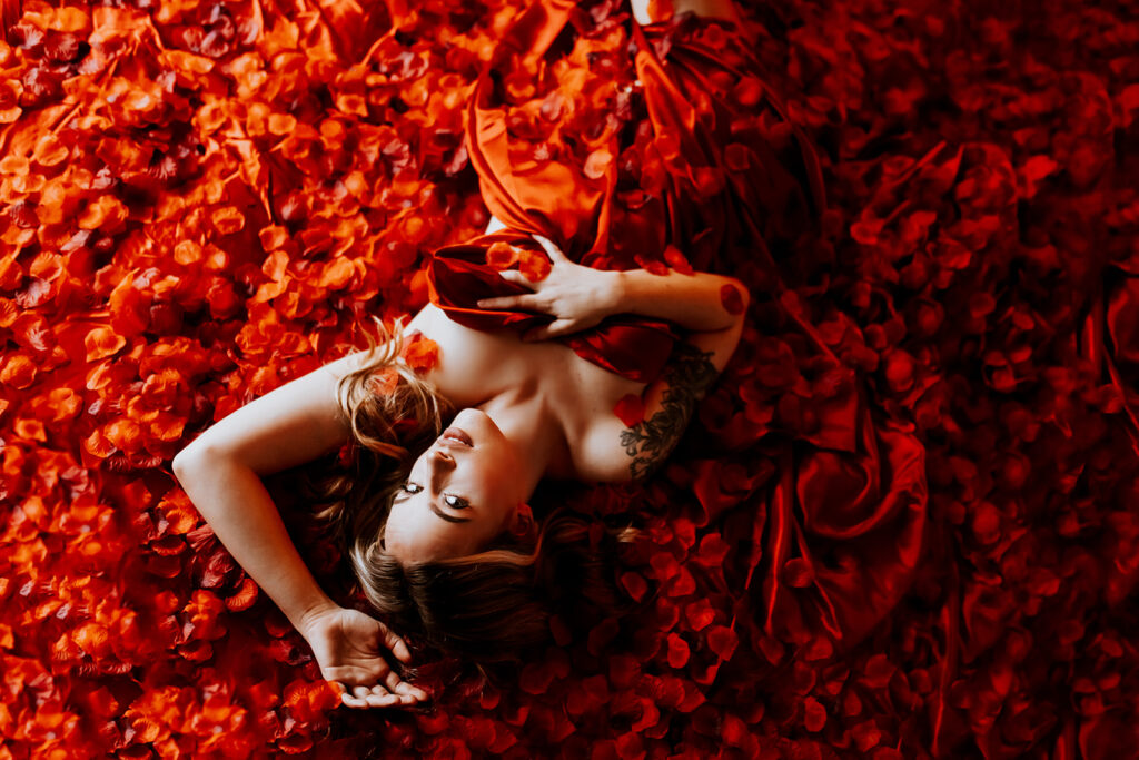 "Luxurious boudoir setting on a red silk bed covered in thousands of red rose petals."
"Sensual moment captured on a velvety red silk bed adorned with a cascade of red rose petals."
"Elegant and romantic boudoir scene featuring a bed covered in red silk and a blanket of rose petals."