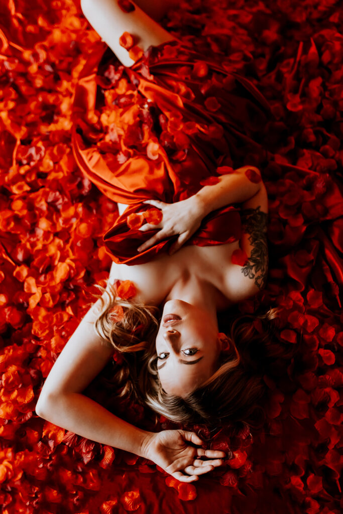 "Luxurious boudoir setting on a red silk bed covered in thousands of red rose petals."
"Sensual moment captured on a velvety red silk bed adorned with a cascade of red rose petals."
"Elegant and romantic boudoir scene featuring a bed covered in red silk and a blanket of rose petals."