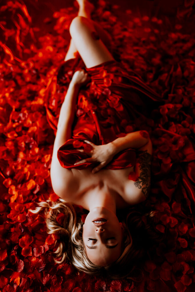 "Luxurious boudoir setting on a red silk bed covered in thousands of red rose petals."
"Sensual moment captured on a velvety red silk bed adorned with a cascade of red rose petals."
"Elegant and romantic boudoir scene featuring a bed covered in red silk and a blanket of rose petals."